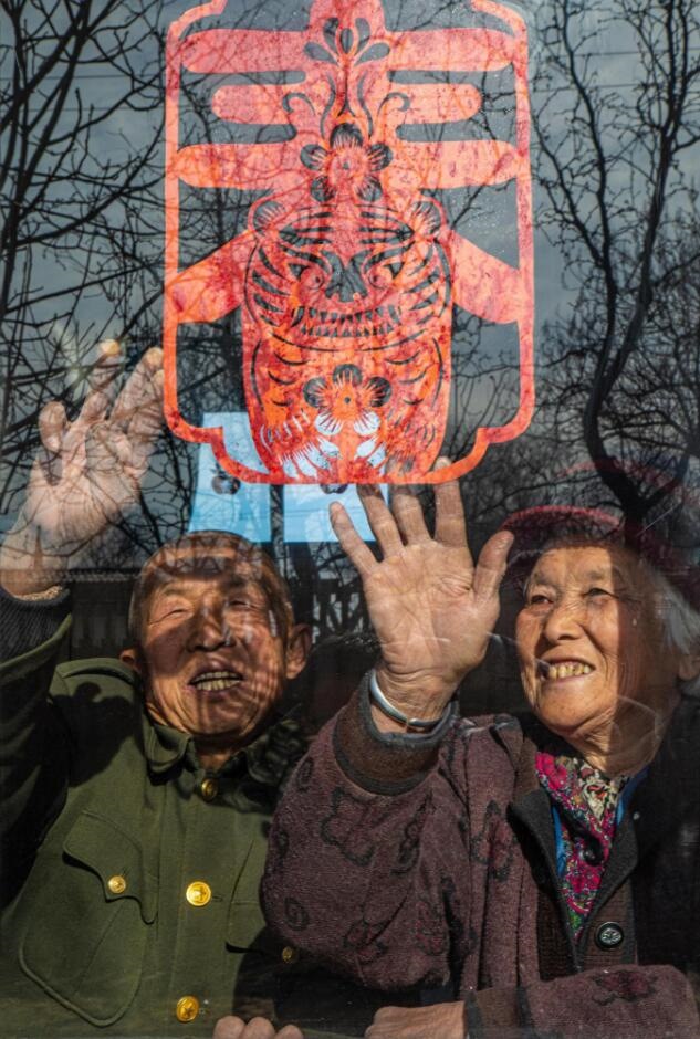 臘月里，霍州市師莊鄉(xiāng)馮南垣村村民師榮光(左)在災(zāi)后重建的新家里貼窗花。(霍州市委宣傳部供圖)