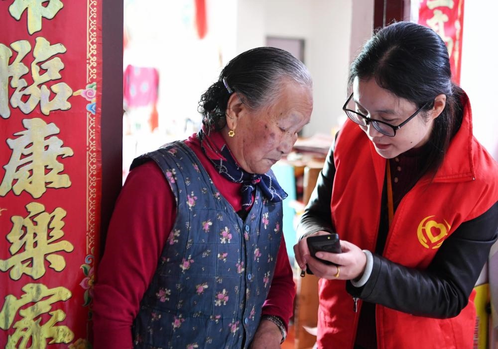 在福州市長樂區(qū)航城街道籌岐村，智慧養(yǎng)老平臺派駐社區(qū)的助老員（右）在為老人陳鳳英（左）講解養(yǎng)老定制手機的用法（2021年11月26日攝）。新華社記者 魏培全 攝