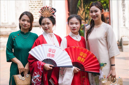 身穿古裝的中國(guó)游客和身穿越南傳統(tǒng)服飾奧黛的越南青年在文廟門前合影。