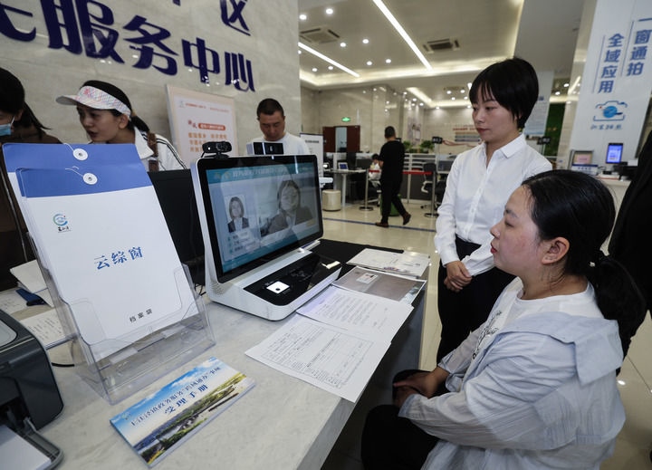 在浙江省嘉興市秀洲區(qū)王江涇鎮(zhèn)便民服務(wù)中心的“跨域通辦·云綜窗”窗口，辦理開業(yè)登記的個(gè)體工商戶（右一）通過(guò)該系統(tǒng)與江蘇省蘇州市吳江區(qū)盛澤鎮(zhèn)行政審批局工作人員視頻連線，進(jìn)行身份讀取及材料線上審核（2024年5月9日攝）。新華社記者 徐昱 攝