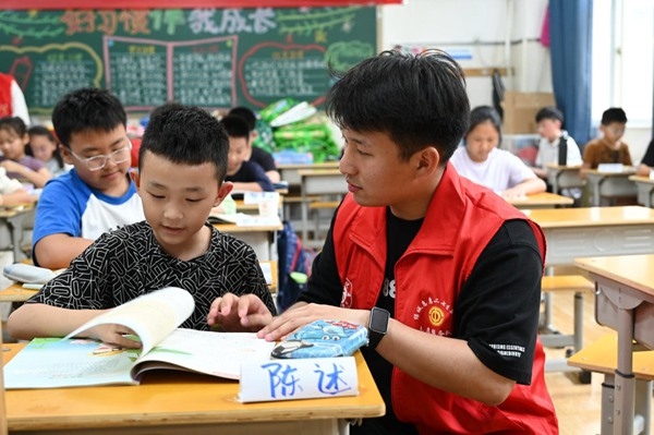 鄭州市二七區(qū)暑托班的志愿者輔導(dǎo)孩子寫(xiě)作業(yè)。人民網(wǎng)記者王玉興攝