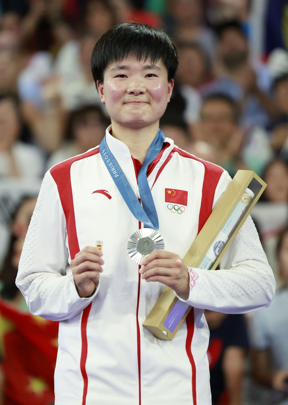 巴黎奧運(yùn)會(huì)羽毛球女子單打亞軍、中國選手何冰嬌在頒獎(jiǎng)儀式上一手握著銀牌，一手握著西班牙奧委會(huì)徽章（2024年8月5日攝）。新華社記者 任正來 攝