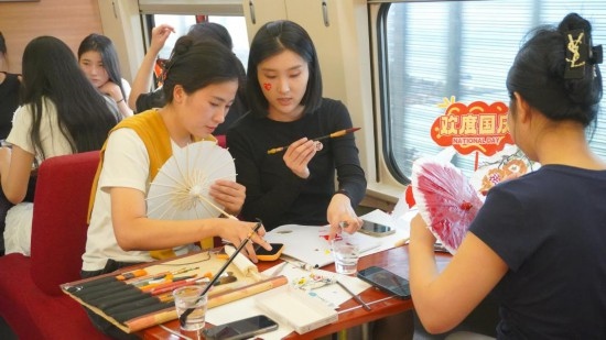 10月1日，旅客們?cè)贕1634次列車(chē)上給油紙傘作畫(huà)。新華社記者周義 攝