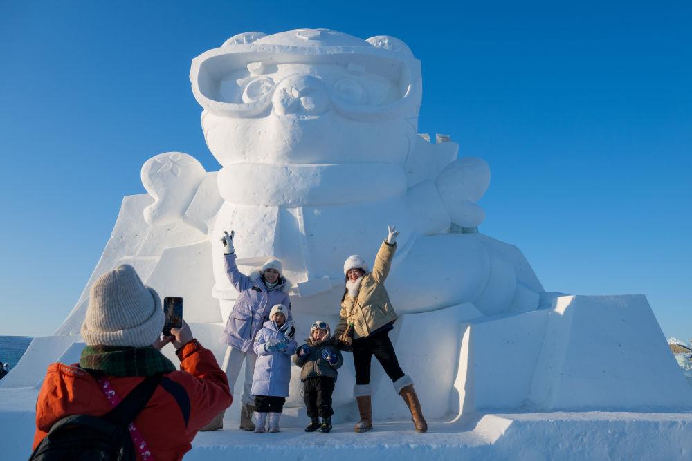 2025年1月3日，在黑龍江哈爾濱冰雪大世界園區(qū)，游客與亞冬會吉祥物雪雕“濱濱”合影